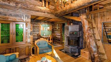 A rustic cabin interior with a stone fireplace, wooden furniture, and a chandelier.