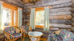 L’intérieur d’une cabane en rondins, avec des meubles en osier, une table ronde et des rideaux aux fenêtres.