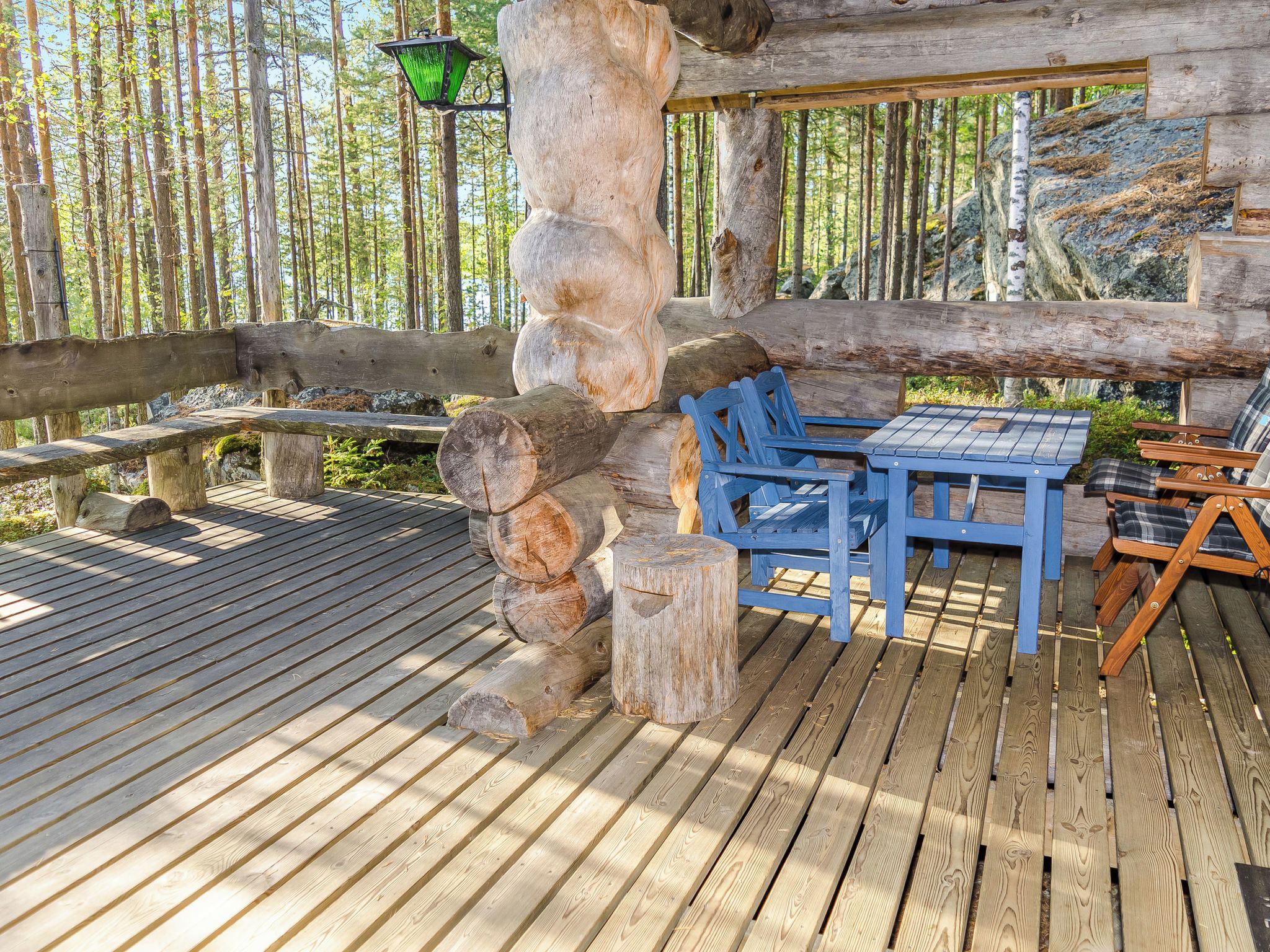 Eine Holzterrasse mit einer rustikalen Steinsäule, einer Bank und einem Tisch mit Stühlen.