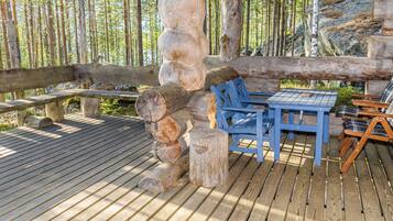 Eine Holzterrasse mit einer rustikalen Steinsäule, einer Bank und einem Tisch mit Stühlen.