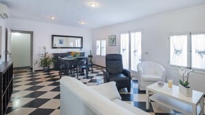 A living room with a checkered floor, a sofa, a chair, a dining table with chairs, and a large mirror. - Voramar 2 by Interhome (Alcúdia)