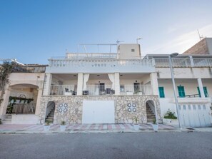 Un edificio de dos pisos con balcón, fachada de piedra y puerta de garaje blanca.