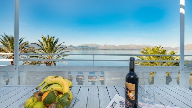A table with a bottle of wine, a fruit bowl, and a placemat with a floral design. - Voramar 2 by Interhome (Alcúdia)