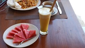 A breakfast setting with a plate of pancakes, a glass of orange juice, a cup of coffee, and a plate of watermelon slices. - Singgahan Bungalow by ecommerceloka (Penida Island)