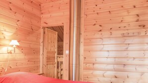 Una habitación tipo cabaña de madera con una cama, una lámpara y una puerta que da a otra habitación.