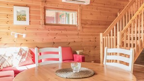 Un interior de cabaña acogedor, con detalles de madera, una mesa de comedor con un mantel tejido, un sofá rojo y una escalera.