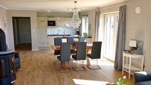 A modern kitchen with white cabinets, a dining area with a wooden table and chairs, a chandelier, and a view of the outside through large windows. - Cottage Country House - Ferienhof Börsby - Cottage Country house (Pommerby)