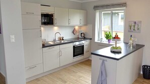 A modern kitchen with white cabinetry, a central island, a built-in oven, and a window with a view. - Cottage Country House - Ferienhof Börsby - Cottage Country house (Pommerby)