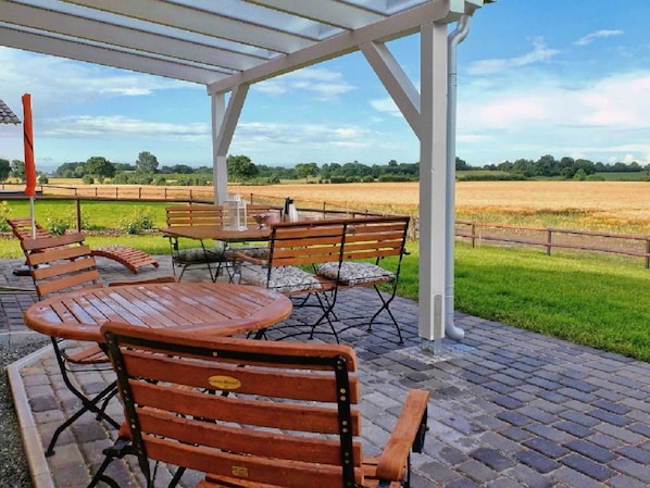 An outdoor patio with wooden furniture and a view of a field.