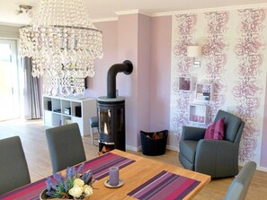 A living room with a modern chandelier, a wood-burning stove, a sofa, and a dining table with a vase of flowers.