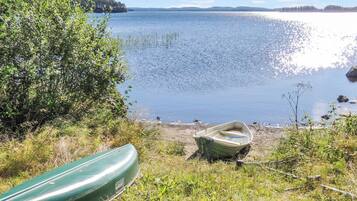 Maisema järven rannalta, jossa näkyy rannalla oleva vene ja toinen vene, joka lepää ruohikolla.