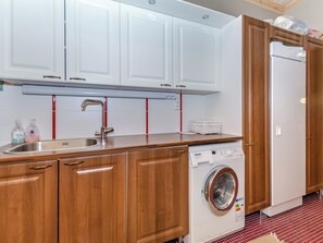 A kitchen with wooden cabinets, a stainless steel sink, a washing machine, and a refrigerator. - Kolin mesikämmen by Interhome (Lieksa)