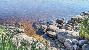 Un lago transparente con rocas y piedras visibles en la orilla.