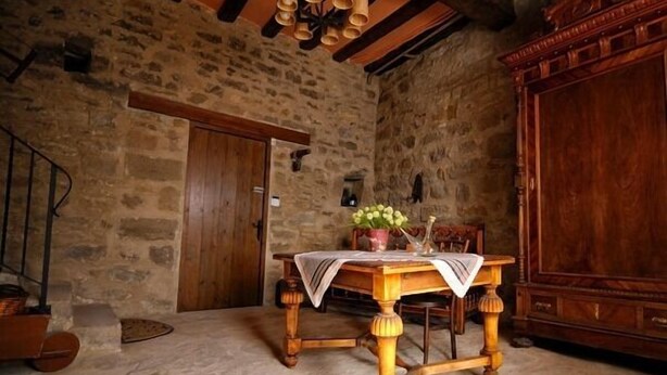A rustic stone-walled room with a wooden table, chairs, and a wooden cabinet. - Rural house (full rental) Masia Pallares de Dalt for 10 people (Olius)
