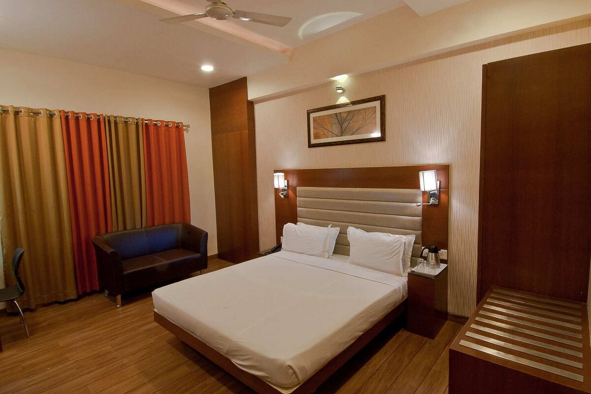 A hotel room with a bed, a nightstand, a lamp, a ceiling fan, and a window with curtains.