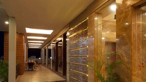 A hallway with a tiled floor, a potted plant, and a table with chairs. - Hotel Imperial (Ujjain)