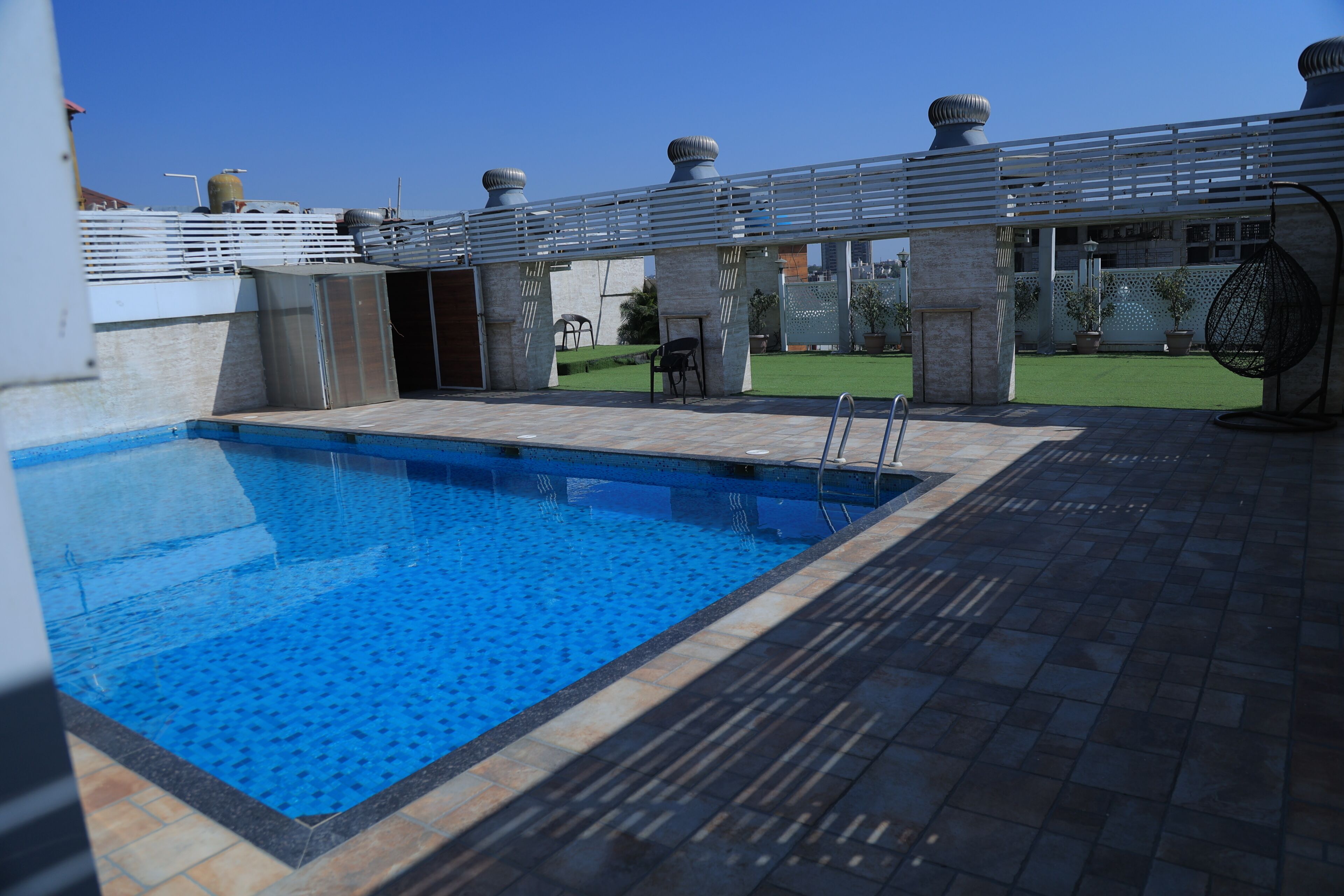 A swimming pool with a tiled deck, a covered seating area, and a view of the cityscape.