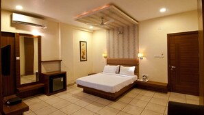 A hotel room with a bed, bedside tables, a mirror, an air conditioner, a ceiling fan, and a door. - Hotel Imperial (Ujjain)