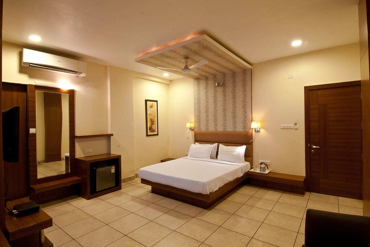 A hotel room with a bed, bedside tables, a mirror, an air conditioner, a ceiling fan, and a door.