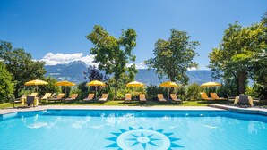 Piscina con diseño de sol, rodeada de sillones de descanso y sombrillas amarillas, con vista a la montaña al fondo.