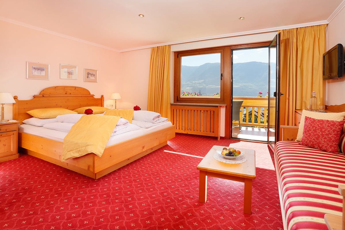 Une chambre d’hôtel avec un lit, un canapé, une petite table, une télévision et un balcon avec vue.