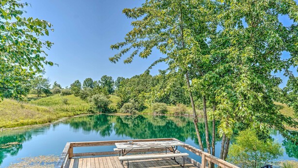 A wooden dock with picnic tables overlooking a calm lake surrounded by lush greenery. - Kimberly's Hope Clark Apt on Farm w/ Pool Access (Clark)