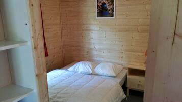 A wooden room with a single bed, a small table, and a framed picture on the wall.