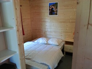 A wooden room with a single bed, a small table, and a framed picture on the wall. - Camping Ibie (Lagorce)