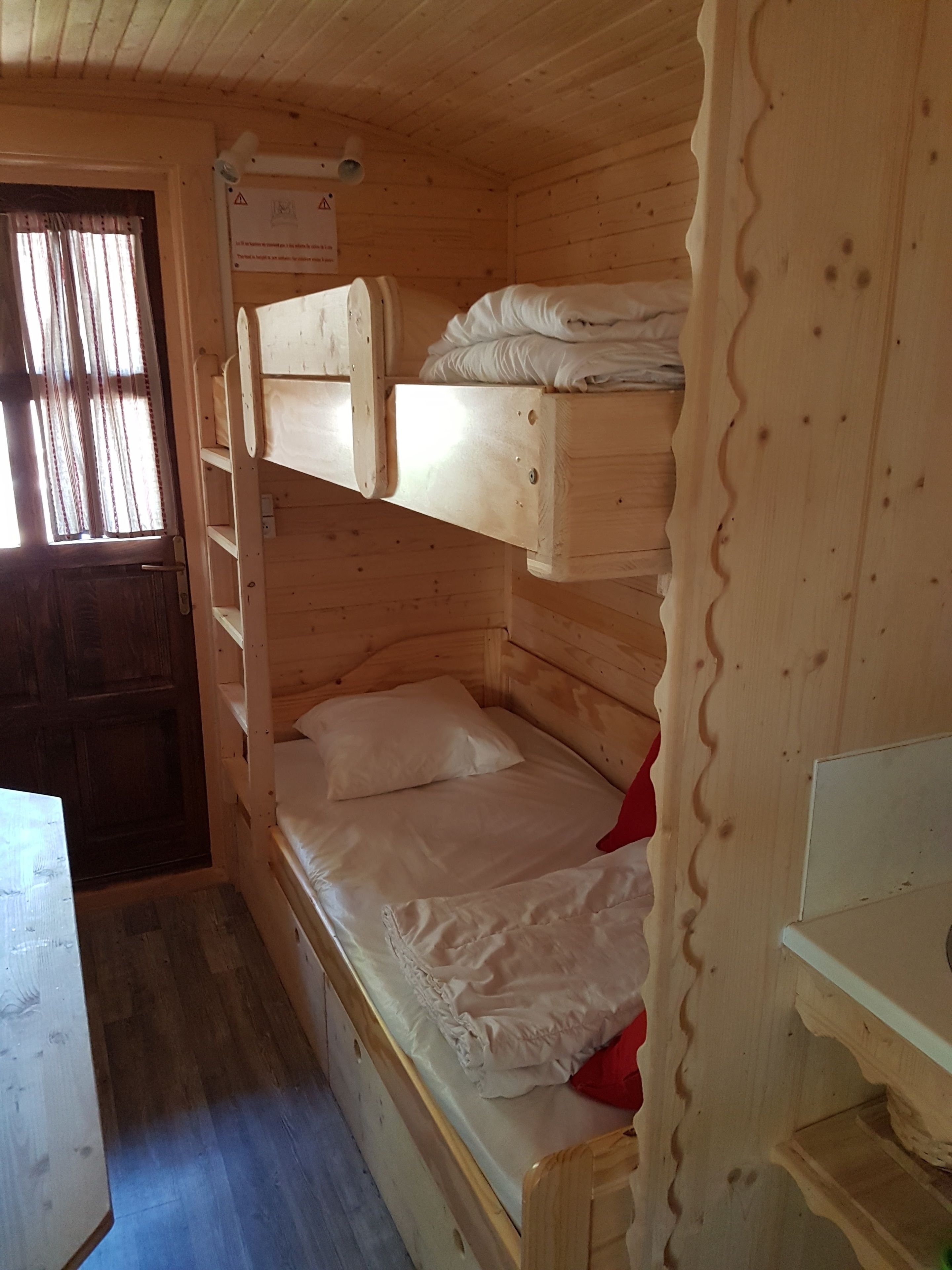 A cabin with a bunk bed, a small desk, and a window with curtains.