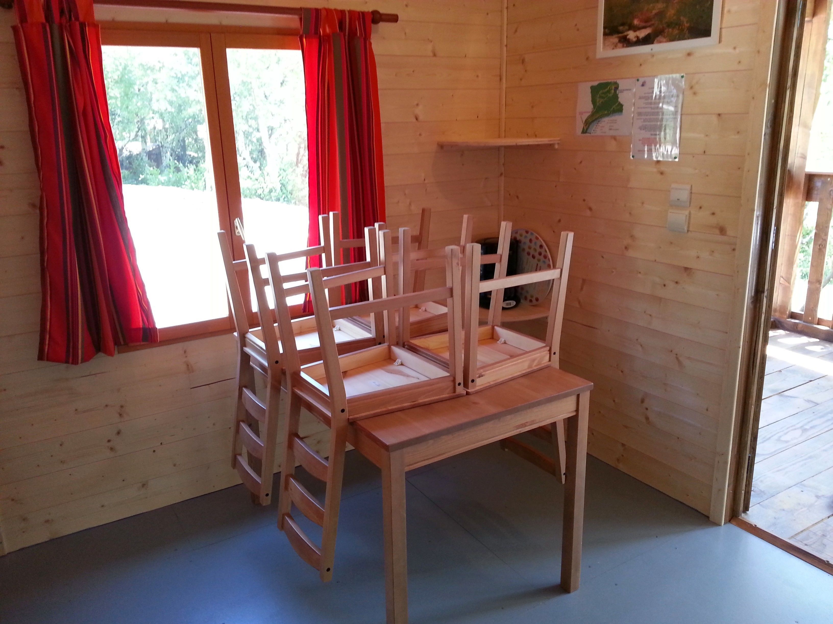 Un interior de madera con una mesa y sillas de madera, cortinas rojas y una ventana con vistas a árboles.