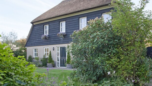 A two-story house with a dark exterior, white window frames, and a thatched roof. - Peace & Space in a real Wieringer residential farmhouse. (Westerland)
