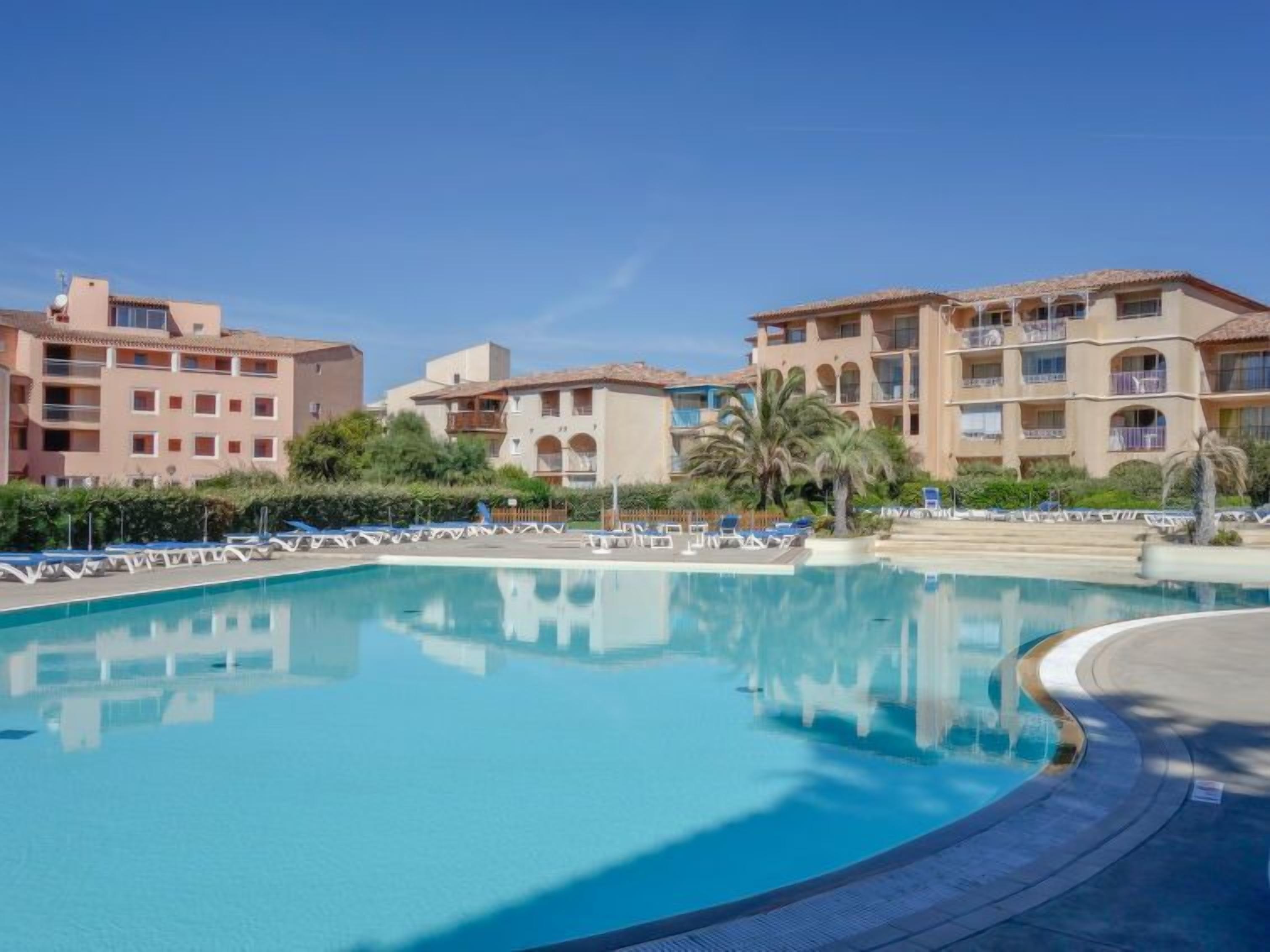 Een zwembad van een resort met helderblauw water, omgeven door palmbomen en ligbedden.