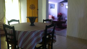 A dining area with a table set for four, a wooden door with a decorative design, and a view into another room with a clock on the wall.