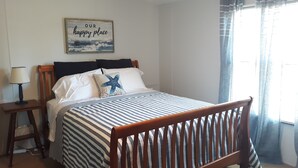 A bedroom with a wooden bed, striped bedding, a starfish pillow, a lamp, and a 'Our happy place' sign. - The Hoi Toider @ Harkers Island (Harkers Island)