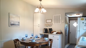 A kitchen with a dining table set for four, a coffee maker, and a refrigerator. - The Hoi Toider @ Harkers Island (Harkers Island)