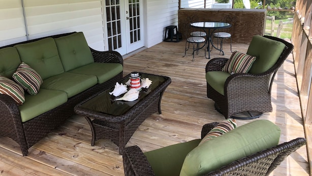 A covered outdoor seating area with a green sofa, wicker chairs, and a table with decorative shells. - The Hoi Toider @ Harkers Island (Harkers Island)