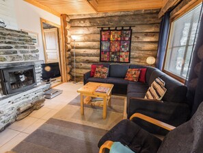 A log cabin interior with a stone fireplace, a dark-colored sofa with patterned cushions, and a wooden coffee table.