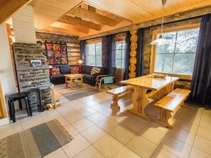 A cozy log cabin interior with a stone fireplace, wooden furniture, and large windows.