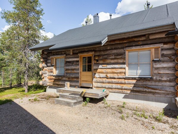 A log cabin with a wooden deck, a front door, and two windows with shutters.