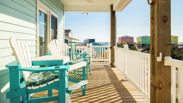 Una terrazza in legno con poltrone Adirondack color turchese e un parapetto bianco.