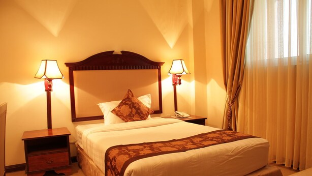 A hotel room with a large bed, two bedside tables, a nightstand, a lamp, and a curtain. - Debredamo hotel (Addis Ababa)