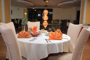 A round dining table with white tablecloth, orange napkins, and a centerpiece. - Debredamo hotel (Addis Ababa)