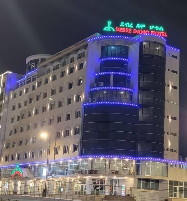 A multi-story hotel with a prominent curved facade, illuminated by blue and white lights. - Debredamo hotel (Addis Ababa)