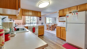 A kitchen with wooden cabinets, a white refrigerator, a microwave, and a dining area with a table and chairs. - 2-Level Home w/ Deck: 1/2 Mi to Lake McConaughy! (Lemoyne)