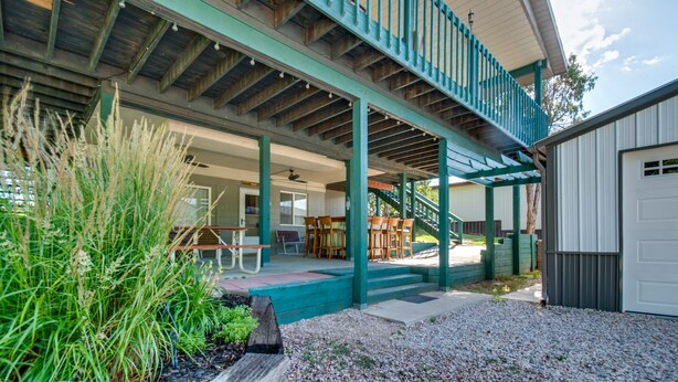A covered outdoor patio with seating, a staircase, and a garage. - 2-Level Home w/ Deck: 1/2 Mi to Lake McConaughy! (Lemoyne)