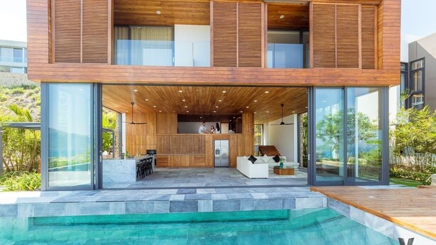 Een moderne villa met een grote glazen gevel, een zwembad en een houten terras.