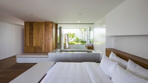 Een moderne slaapkamer met een groot bed, een houten accentmuur, een glazen douche en uitzicht op groen buiten.