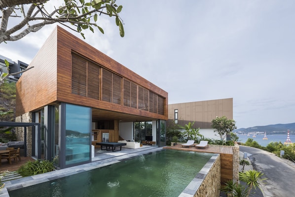A modern house with a swimming pool, outdoor seating, and a view of the sea.