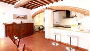 A kitchen with a brick arch, wooden ceiling beams, a dining table, and bar stools. - "Il Focolare" Superior Apartment in Monticchiello (Monticchiello)