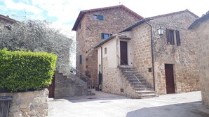A stone building with a staircase leading to a door, surrounded by a hedge and a cobblestone ground. - "Il Focolare" Superior Apartment in Monticchiello (Monticchiello)